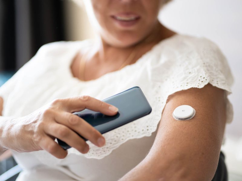 Woman Testing Glucose Level With Continuous Glucose Monitor On Mobile Phone