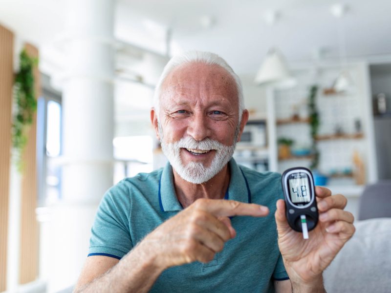 Blood sugar testing at home. Checking Blood Sugar Level At Home. Diabetic Checking Blood Sugar Levels. Senior man checking blood sugar level by glucometer and test stripe at home